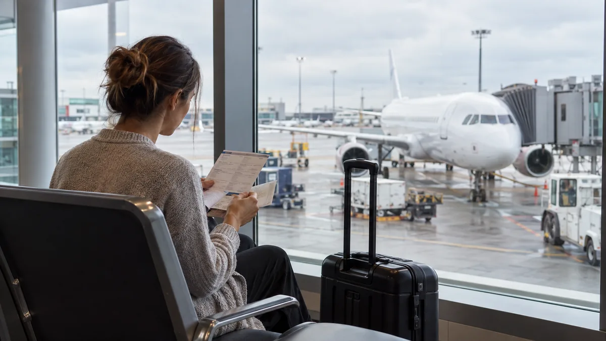 Traveler reviewing documents beside a cabin suitcase at an airport window